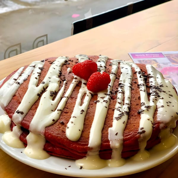 Red velvet pancakes with white chocolate drizzle, chocolate shavings, and fresh raspberries at Breakfast Club.