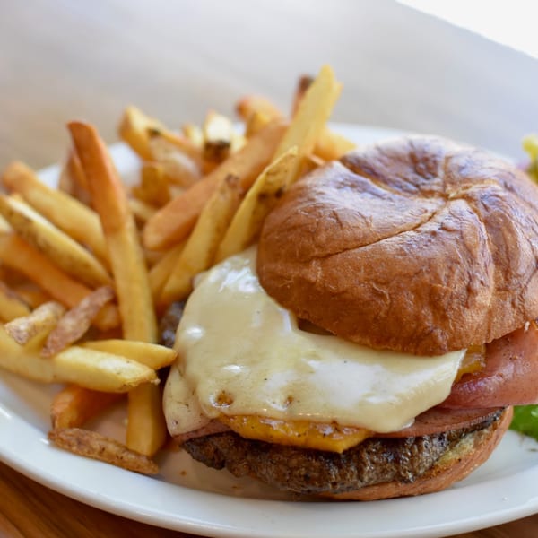 Breakfast Club burger with melted cheese, bacon, and a side of golden french fries on a white plate.