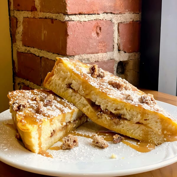 Two slices of French toast with caramel, pecans, and powdered sugar on a white plate.