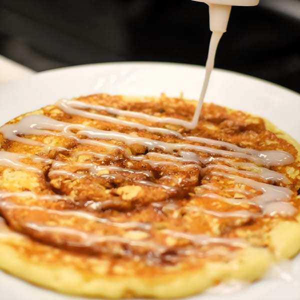 A Breakfast Club pancake, drizzled with white icing from a squeeze bottle.