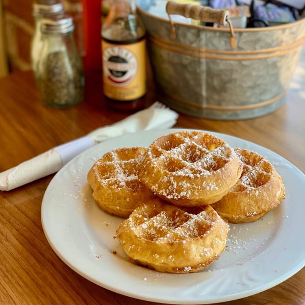 Four golden waffles dusted with powdered sugar on a white plate at Breakfast Club.