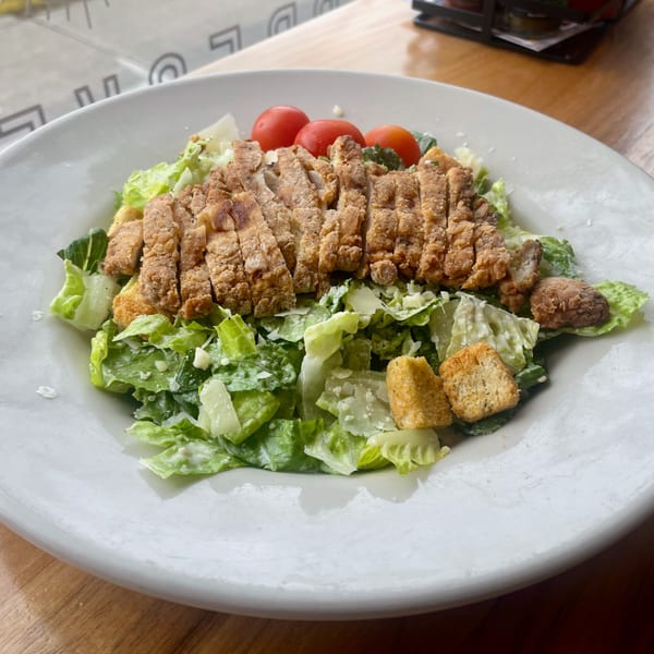 A Caesar salad with crispy fried chicken, cherry tomatoes, croutons, and parmesan cheese.